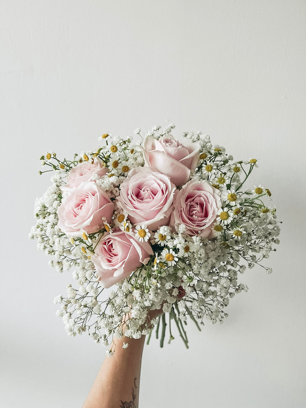 Bouquet of pink roses and baby's breath held against a light background