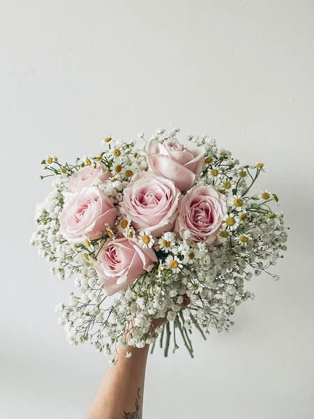 Bouquet of pink roses and baby's breath held against a light background