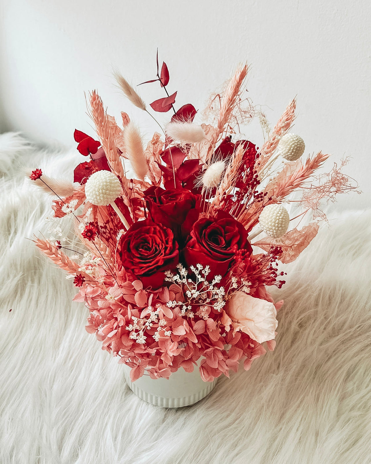 Bouquet of red and pink flowers in a white vase on a fluffy white surface