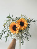 Bouquet of sunflowers and greenery held by a person against a light gray background