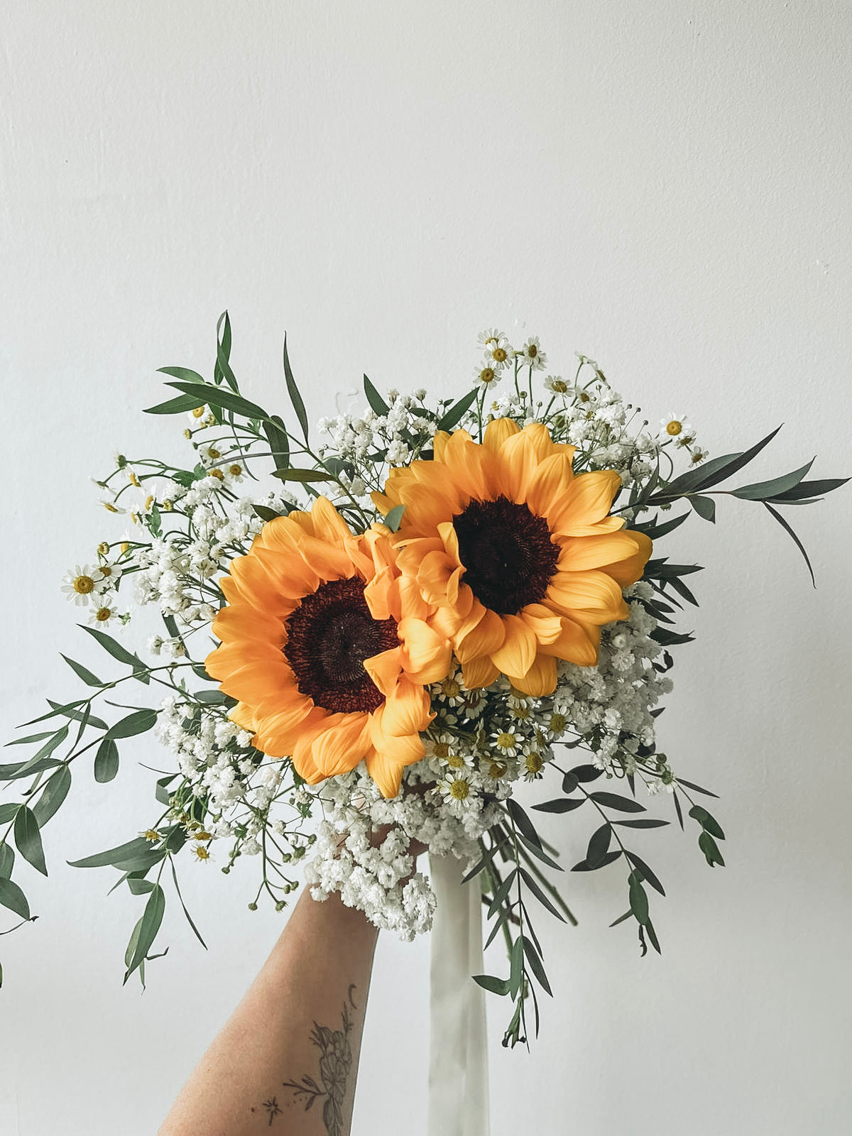 Bouquet of sunflowers and greenery held by a person against a light gray background
