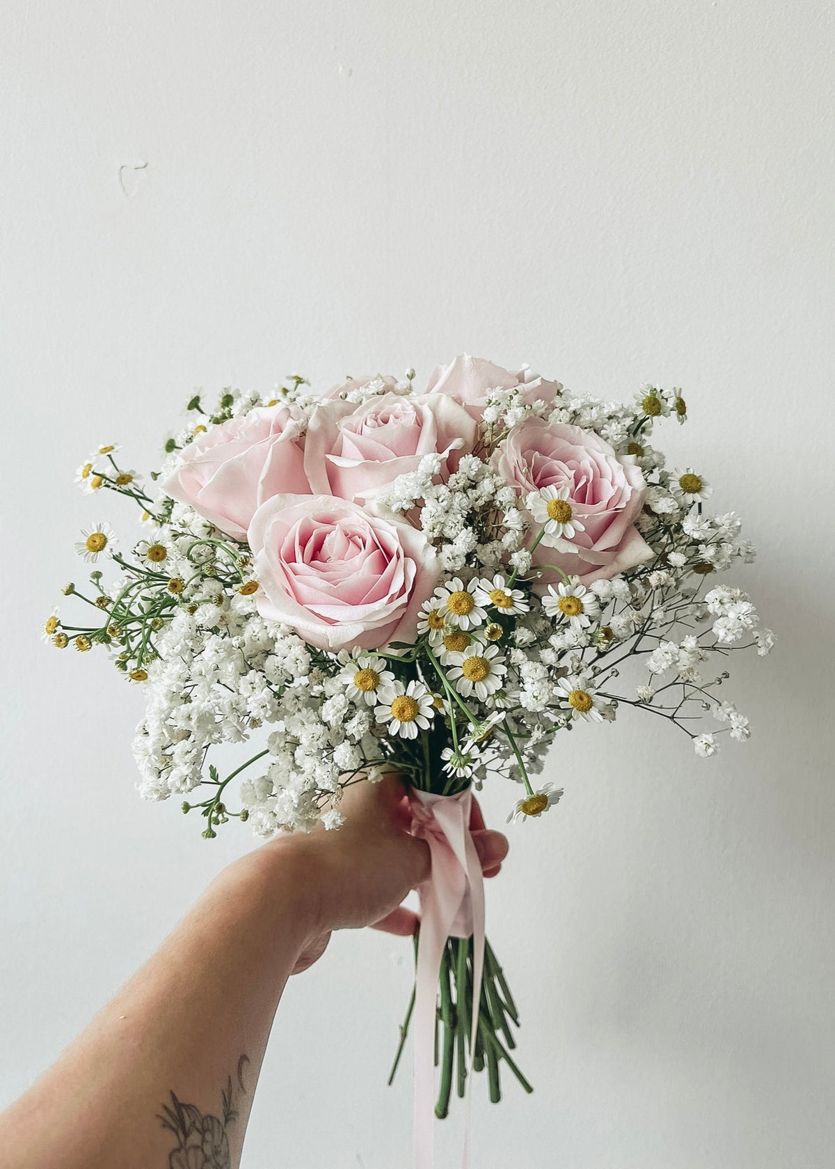 Bouquet of pink roses and baby's breath held by a hand against a light background