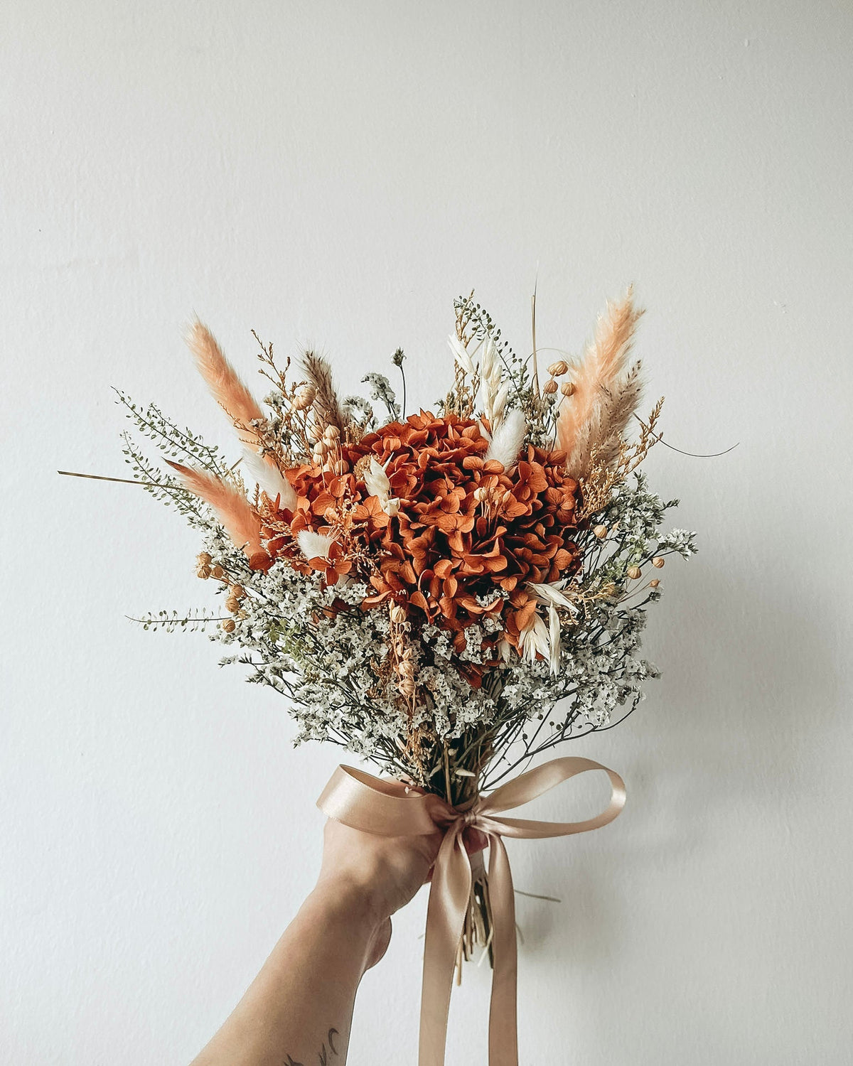 Bouquet of dried flowers with a beige ribbon held against a light background