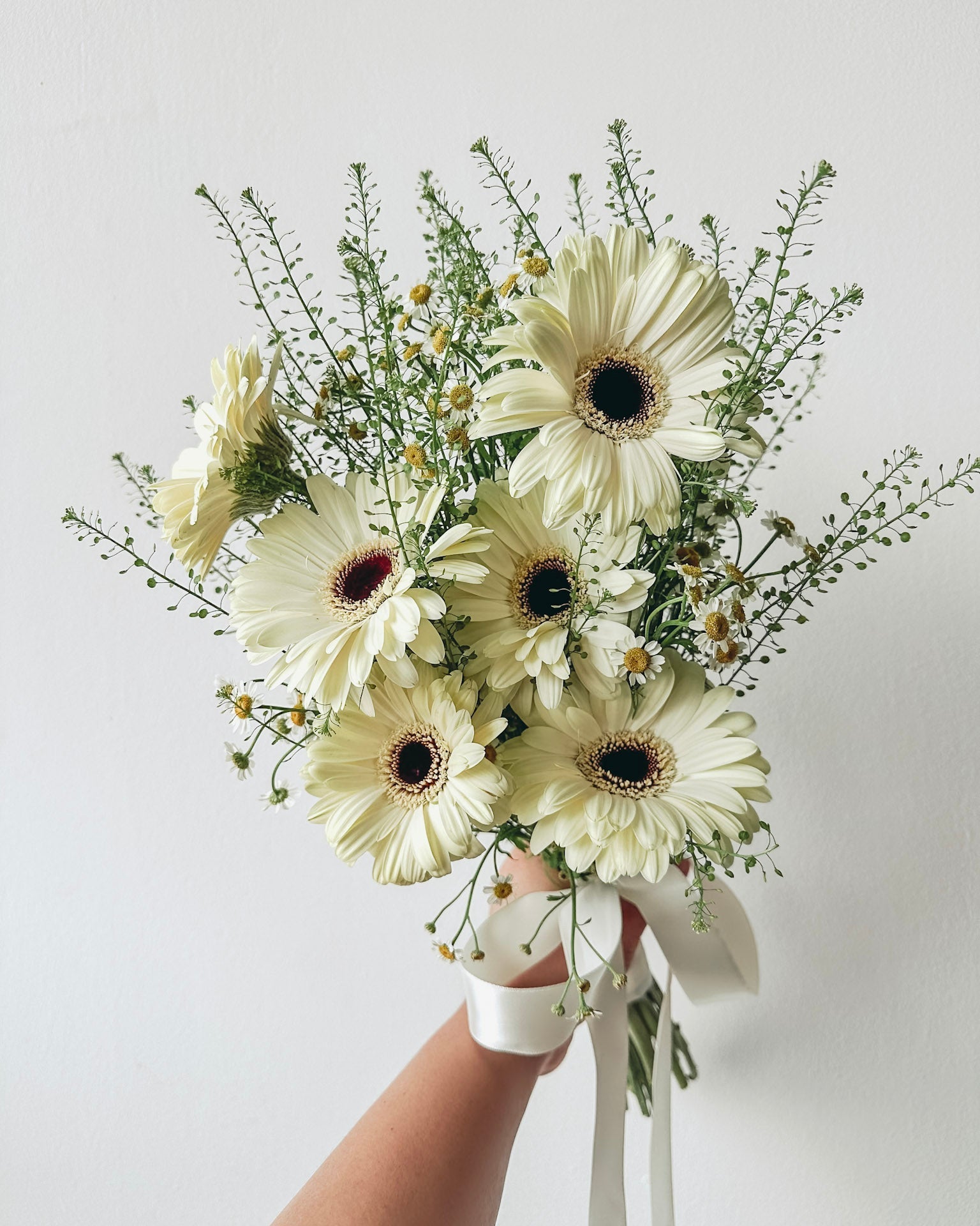 Bouquet of white flowers held by a hand against a light gray background